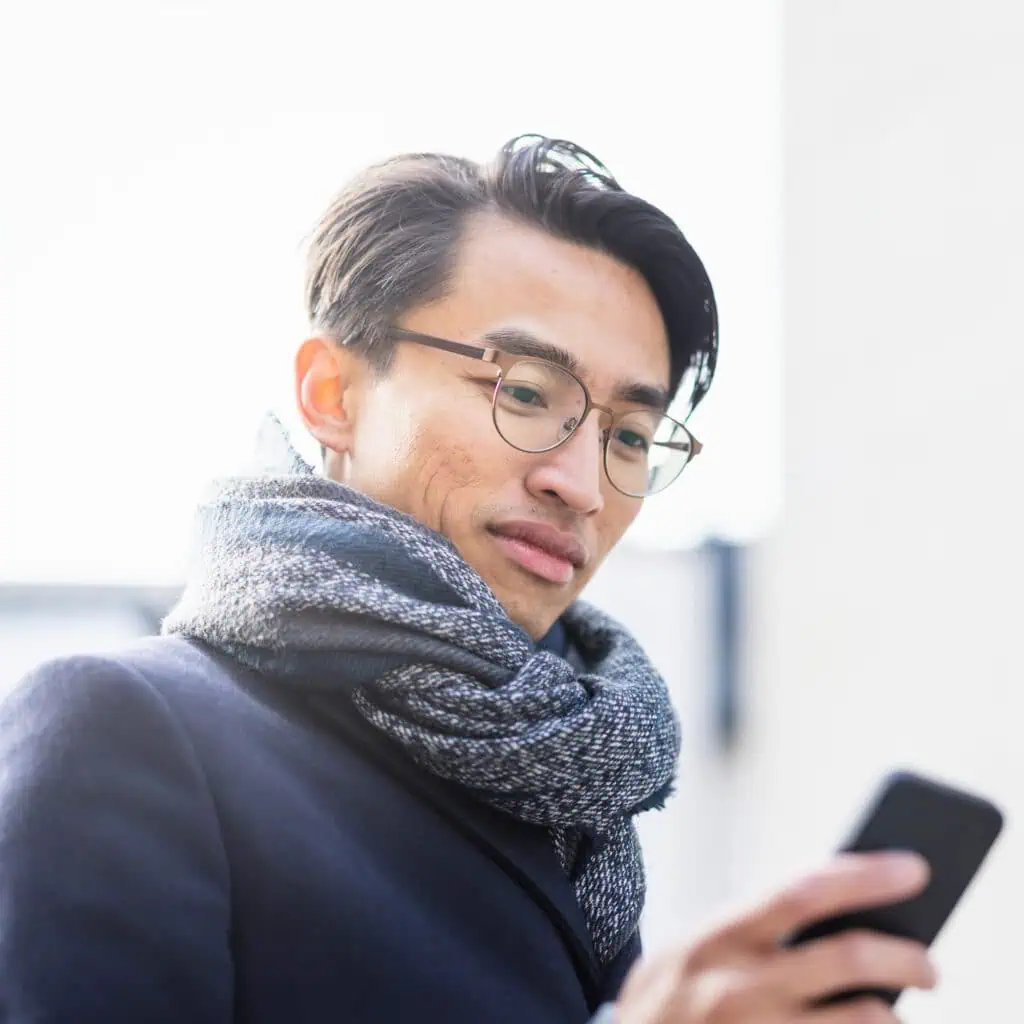Skön man med glasögon och halsduk som använder mobiltelefon utomhus.