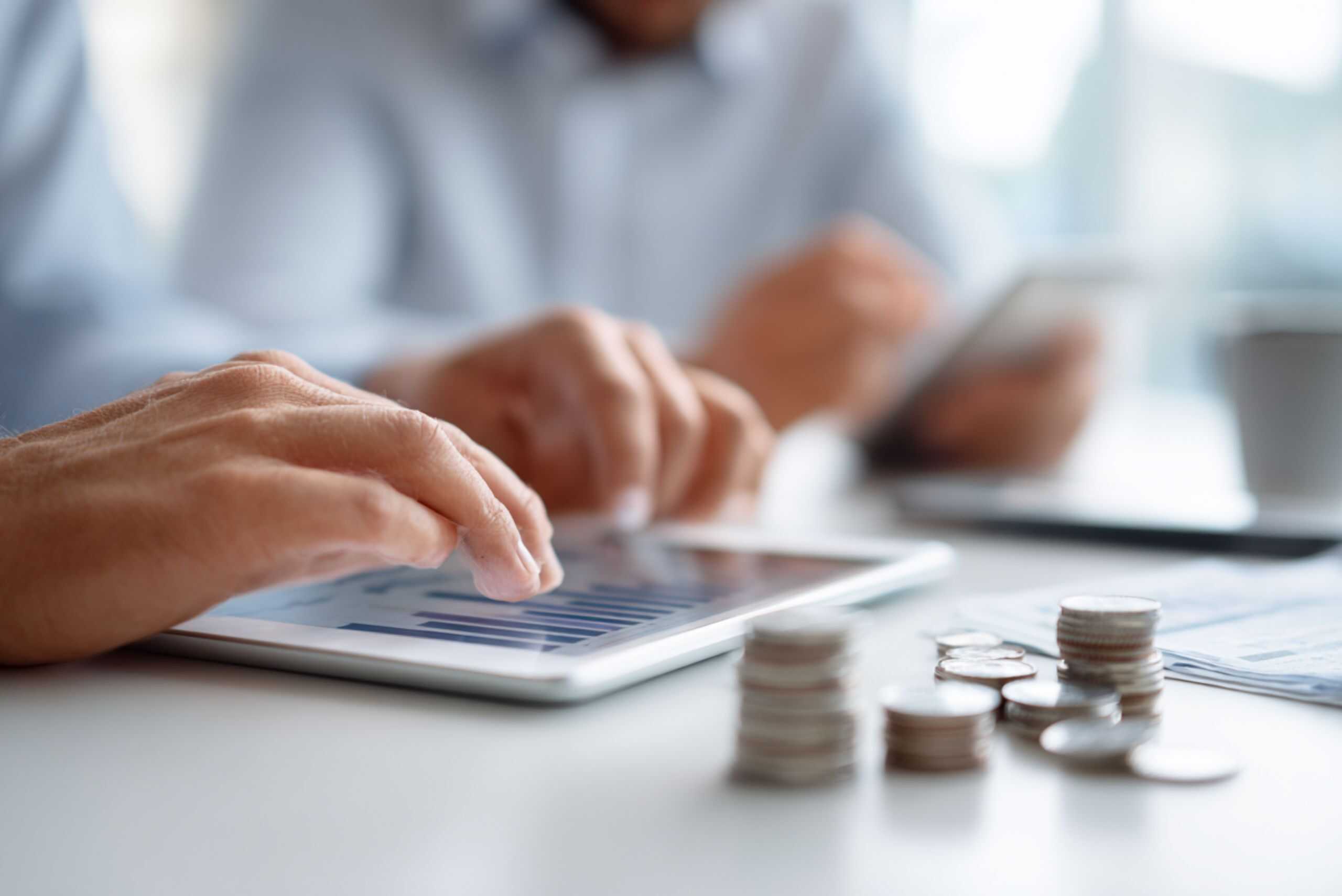 1. Person som gör ekonomi- och finansarbete med surfplatta och mynt på bordet.