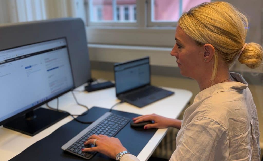 Kvinna arbetar vid dator i kontorsmiljö med två skärmar.